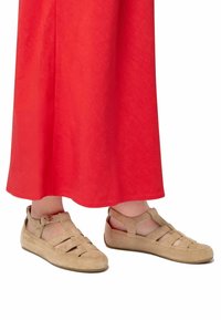 Sandales en suède beige au design ouvert, dotées de plusieurs lanières, d'une boucle et d'une texture douce, associées à une jupe rouge.