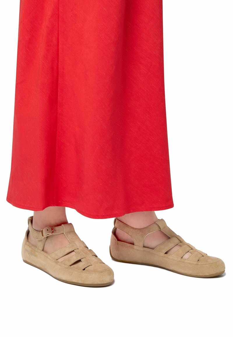 Světlé semišové sandály s otevřeným designem, které mají několik pásků, přezku a jemnou strukturu, spárované s červenou sukni.