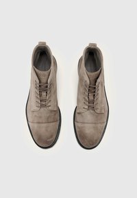 Wildleder-Stiefeletten in Hellgrau mit Schnürdesign, abgerundetem Zehenbereich und kontrastierender schwarzer Gummisohle. Glatte Textur mit praktischem Zuglasche am Schaft.