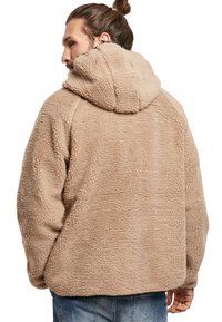 Sudadera con capucha color beige de felpa, con una superficie texturizada y esponjosa. El diseño es de estilo oversize, con un corte recto y sin cierres visibles.