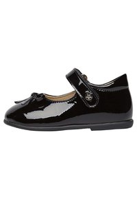Zapato Mary Jane de charol negro con punta redonda, lazo decorativo y correa ajustable que presenta un botón metálico en forma de estrella.