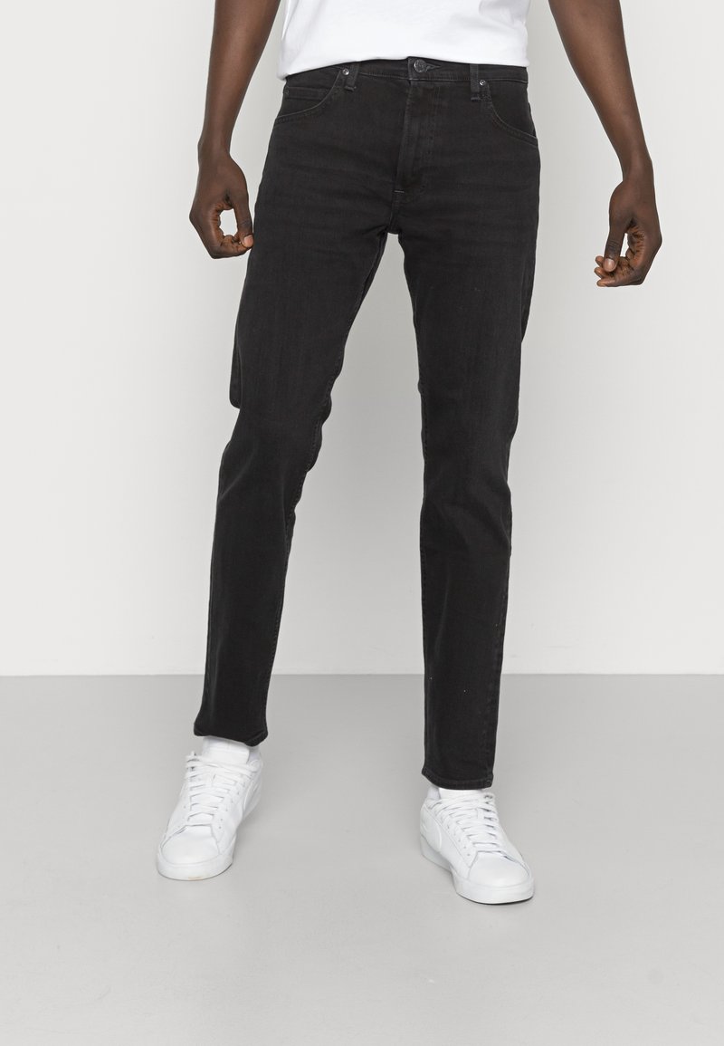 Svarta denimjeans i slim fit, med kontrasterande sömmar, fem fickor och traditionell knapp- och dragkedja. I kombination med vita sneakers.
