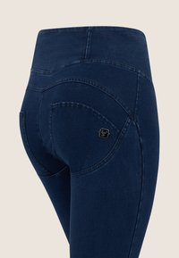 Marineblauwe jeans met een hoge taille en gebogen achterzakken. Voorzien van een zwart merketiket en een soepele, rekbare denimstof.