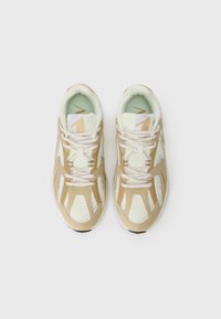 Zapatillas deportivas en tonos beige y blanco, fabricadas con materiales de malla y cuero. Las características incluyen una parte superior texturizada, cordones contrastantes y una plantilla de color menta.