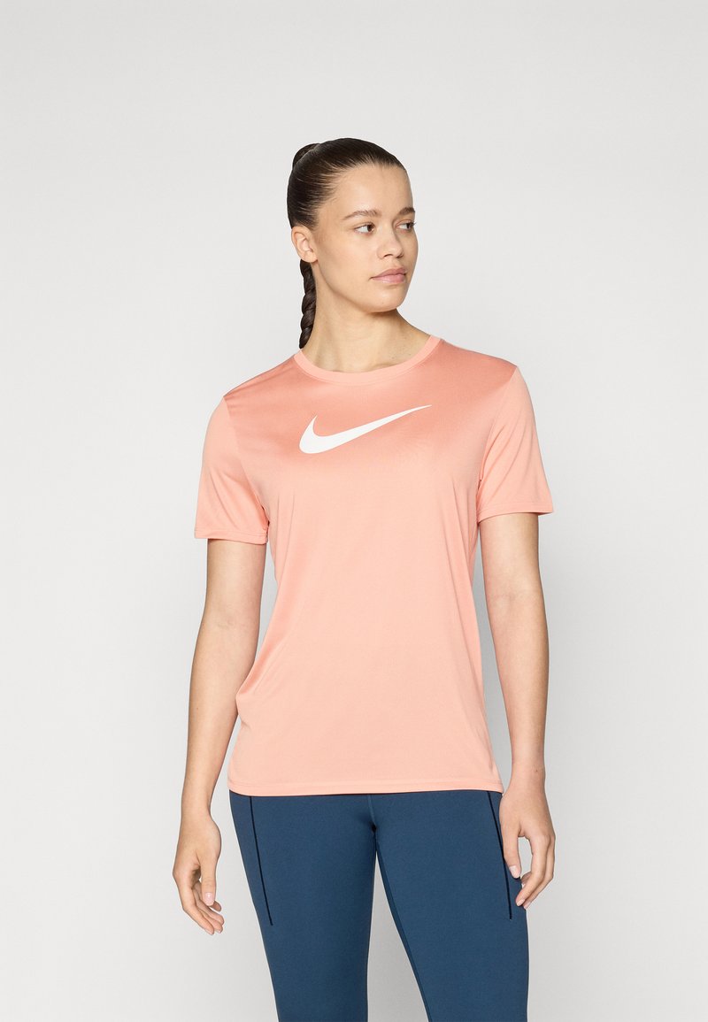 Vaate t-paita, lyhythihainen ja pyöreäkauluksinen Nike, vaaleanpunaisesta kankaasta, jossa on suuri valkoinen Nike-logo rinnan kohdalla. Sileä tekstuuri, minimalistinen muotoilu.