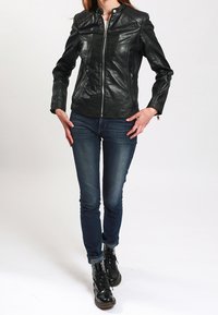 Černá kožená bunda se zipem vpředu, s vysokým límcem a strukturovanými rameny. Kombinováno s tmavě modrými džínami a černými kotníkovými botami na šněrování.