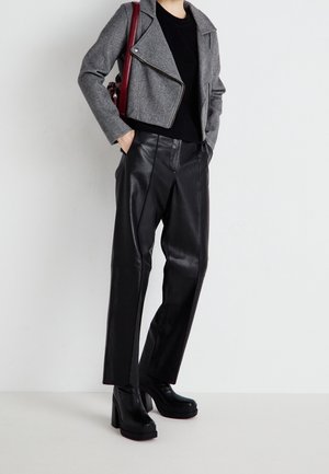 Person wearing black platform boots, black leather pants, black top, and gray cropped jacket with hands in pockets, carrying red shoulder bag.