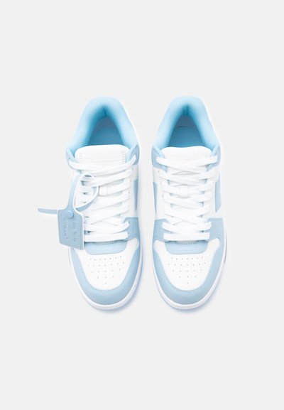 Ζευγάρι λευκά και ανοιχτό μπλε αθλητικά παπούτσια με λευκά κορδόνια, ετικέτα προσαρτημένη στο αριστερό παπούτσι, εμφανίζεται από πάνω σε απλό φόντο.