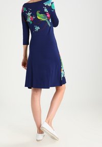 Marinblå klänning med trekvartslånga ärmar. Har livfulla blom- och fågelmönster på ryggen och en avslappnad passform. Slutar ovanför knäet.