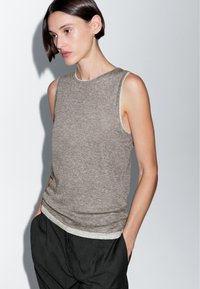 Top grigio senza maniche con una finitura testurizzata e bordi chiari, abbinato a pantaloni neri; presenta un collo a giro e un design rilassato.