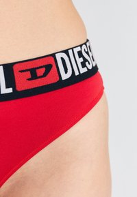 Brief en coton rouge avec une large ceinture noire portant l'inscription et le logo blancs "DIESEL", texture lisse et design ajusté.