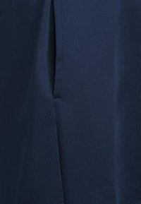 Marineblåt stof med en glat tekstur, der har en sidelomme og ren syning. Materialet virker let og blødt.