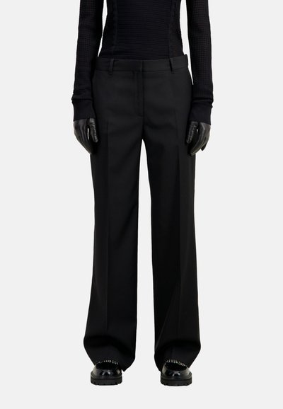 Pantalones negros ajustados con un diseño de pierna recta, que cuentan con una cinturilla limpia y bolsillos laterales, combinados con guantes negros.