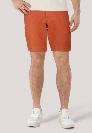 Rostfarbene Baumwoll-Shorts mit geradem Schnitt und Saum, kombiniert mit weißen Sneakers mit Mesh- und Lederelementen.