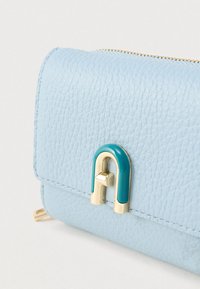 Šviesiai mėlynas odinis piniginė su tekstūruota apdaila, priekyje su auksiniu ir turkio spalvos sagties akcentu. Viršuje užsegama užtrauktuku.
