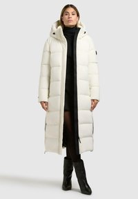Lange, puffy witte jas met een capuchon, voorzien van een ritssluiting, zijritsen en een zwart accent aan de voorkant.