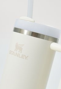 White insulated tumbler with a stainless steel band, clear lid, and a straw. Features the "STANLEY" logo and a smooth matte finish.