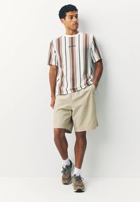 Striped short-sleeve t-shirt in white, brown, and beige with "ROMA" embroidered; paired with beige shorts and brown sneakers with accents.