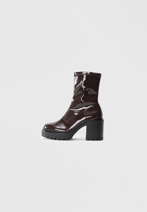 Glossy burgundy ankle boot with a chunky black heel, featuring a smooth texture and simple design. No visible fastenings or patterns.