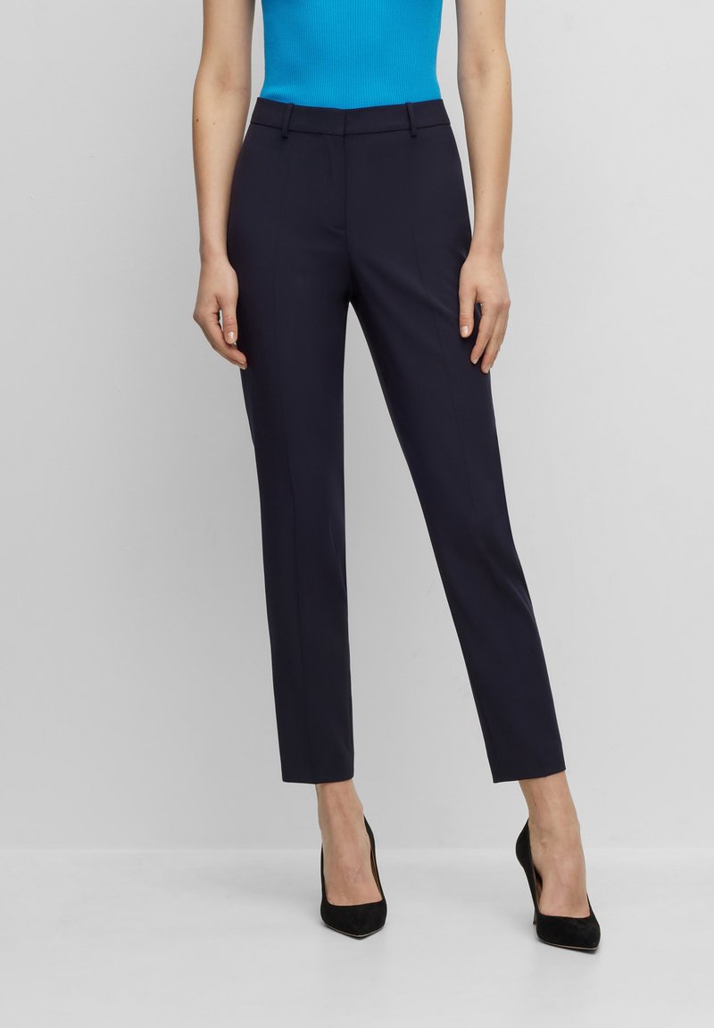 Pantalones de traje azul marino con un corte ajustado, lazos para cinturón y bolsillos laterales. Textura de tela suave y detalles de costura precisos.