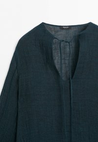 Dark teal textured long-sleeve blouse with a round neckline and tie closure, made of lightweight fabric, label reads Massimo Dutti.