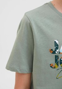 Svijetlozelena pamučna majica s kratkim rukavima, koja sadrži šareni grafički otisak s tekstom. Ima okrugli izrez i glatku teksturu.