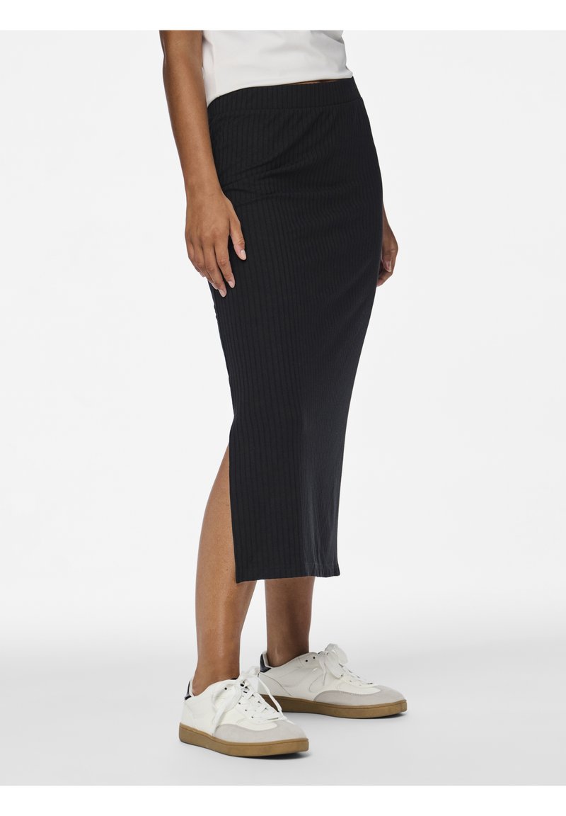 Falda midi de punto negro acanalado con abertura lateral y cintura elástica, combinada con zapatillas blancas con detalles marrones.