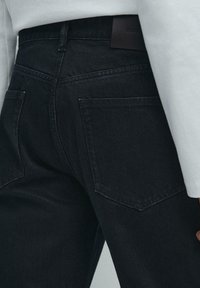 Jeans in denim nero con una texture liscia, dotati di due tasche posteriori, una patch in pelle sulla vita e un design aderente.