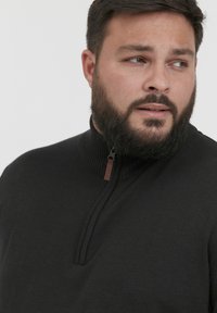 Must kollane kootud pusa, millel on kõrge kaelus ja lukuga eesosa. Omab soonikstruktuuri ja väikest pruuni aktsenti lukul.
