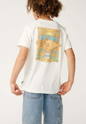 Niño con pelo rizado que lleva una camiseta blanca con un gráfico colorido de temática de surf y pantalones cortos vaqueros azul claro, de pie con la espalda hacia la cámara.