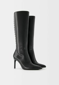 Knähöga svarta läderstövlar med klack, spetsig tå och dekorativa knappdetaljer längs den yttre sidan. Slät textur och elegant design.