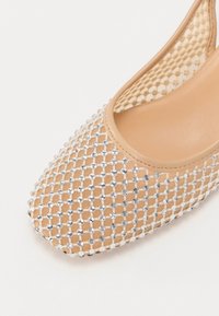 Bēša auduma kurpes ar sietveida dizainu, rotātas ar mazām sudraba toņu rhinestones, ar gludu bēšu odere un noapaļotu purngalu.