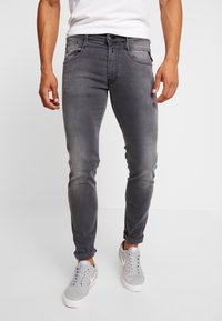 Vaqueros ajustados gris con textura descolorida, diseño de cinco bolsillos y dobladillos remangados, combinados con zapatillas deportivas gris claro. Camiseta blanca debajo.