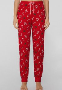 Rode pyjamabroek gemaakt van zachte stof, met witte zuurstokken en groene hulstpatronen. Voorzien van een elastische tailleband en een trekkoord.