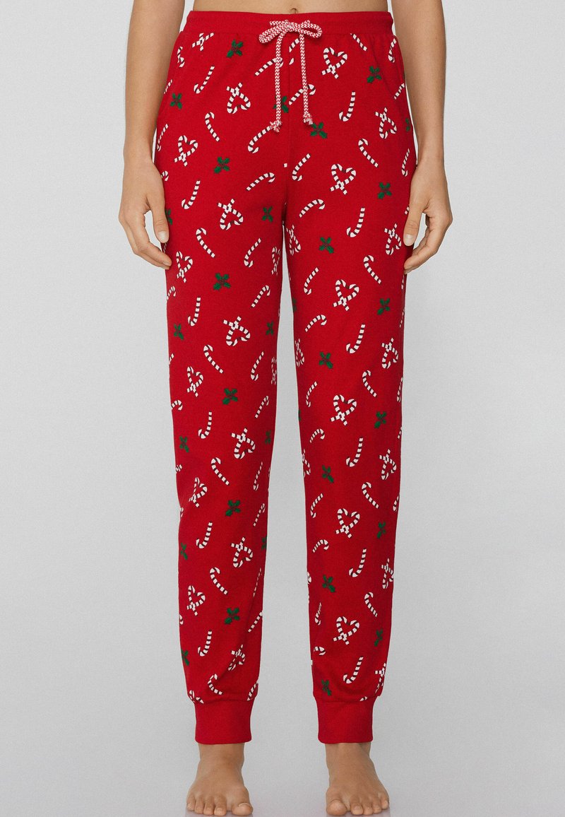 Rode pyjamabroek gemaakt van zachte stof, met witte zuurstokken en groene hulstpatronen. Voorzien van een elastische tailleband en een trekkoord.