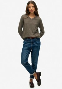 Szary sweter w serek, niebieskie dżinsy z podwiniętymi nogawkami i bordowe buty. Sweter ma miękką strukturę; dżinsy to klasyczny deniming. Buty mają masywną podeszwę.