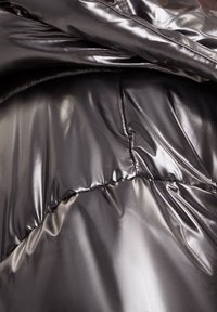 Svart puffjacka med blanka material, quiltat mönster med synliga stygn och en jämn yta. Accentuera med en slät finish.