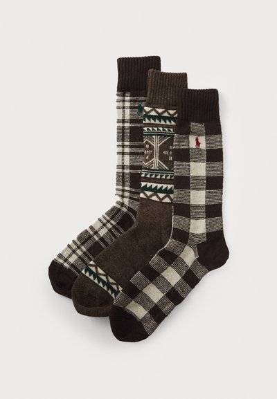Tre par med strikkede sokker i ulike brune nyanser. Mønstre inkluderer striper, ruter og geometriske design. Ribbestrikkede mansjetter og logo-aksenter.