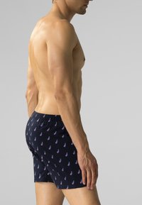 Granatowe bokserki wykonane z lekkiego materiału z powtarzającym się wzorem fioletowych bakłażanów. Widoczny elastyczny pas.