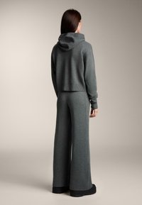 Šedá pletená mikina s širokým golierom, skrátený strih, v kombinácii s ladícími širokými nohavicami. Hladká textúra, minimálne kovanie, uvoľnený strih.