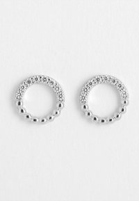 Silverfärgade cirkulära örhängen med en texturerad pärldesign. En kant har små klara kristaller för extra detaljer.