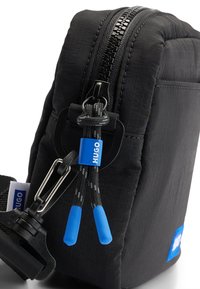 Bolsa de nylon negra de forma rectangular, con un zipper resistente, acentos en azul, superficie texturizada y una etiqueta de la marca.