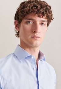 Himmelblaues Button-Down-Hemd mit strukturiertem Kragen, ausgestattet mit einem glatten Stoff und dezenten Details auf der Unterseite des Kragens.
