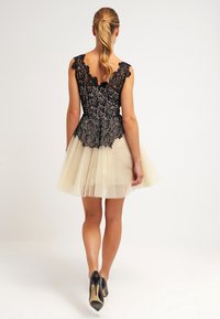 Robe à top en dentelle noire avec jupe en tulle beige. Caractérisée par un corsage ajusté et un ourlet évasé. Des chaussures noires à talons hauts complètent le look.