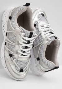Baskets en maille argentée et synthétique avec des lacets blancs, des accents noirs et une semelle blanche mouchetée. Forme arrondie, texture respirante.