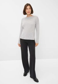 Grauer Langarmpullover mit Rundhalsausschnitt, kombiniert mit schwarzen weiten Hosen. Glatte Textur, dezente Seitendetails und Passform. Schwarze Schuhe.