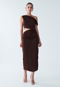 Abito marrone con una spalla, caratterizzato da un taglio in vita e da una texture arricciata. Abbinato a sandali dorati con cinturini. Design senza cuciture, lunghezza fino al pavimento.