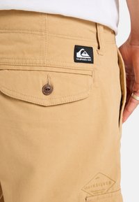 Krémové látkové šortky s látkovou nášivkou s logem Quiksilver, zapínání na knoflík a strukturovaný pas.