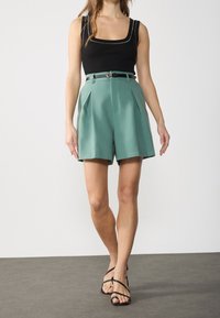 Débardeur noir à encolure carrée associé à un short plissé vert menthe et une ceinture noire étroite, présentant un tissu lisse et une coupe ajustée.