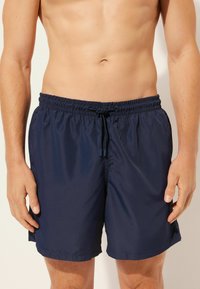 Mörkblå badshorts gjorda av lätt material, med ett elastiskt midjeband och dragsko. Enkelt mönster, inga mönster eller detaljer.